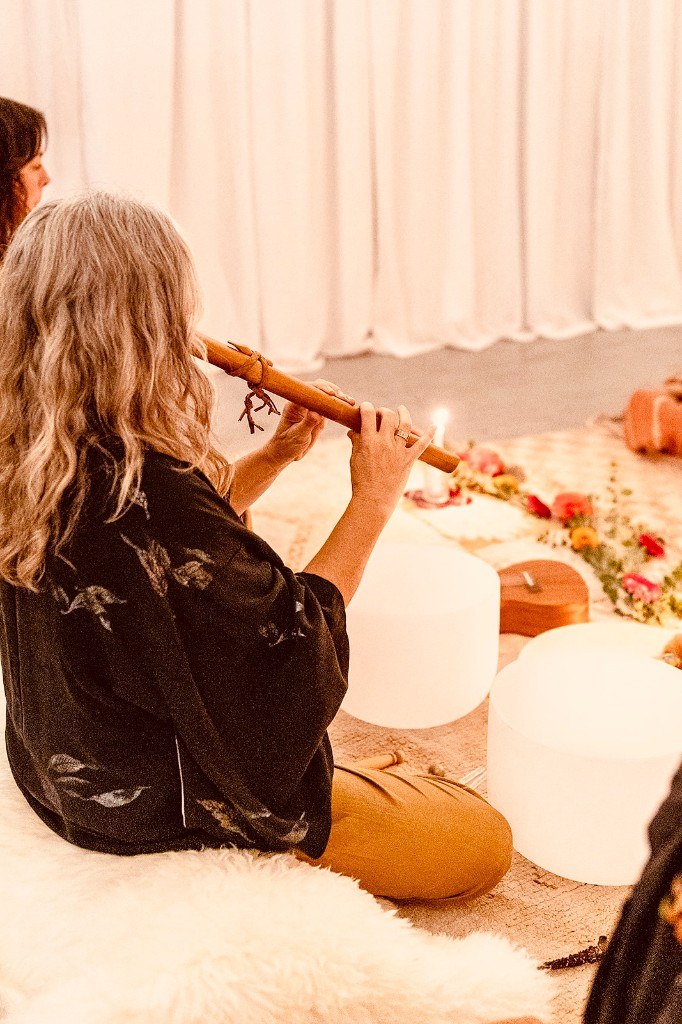 Amanda playing wooden flute during a sound healing session with crystal singing bowls